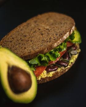 Delicious rye bread sandwich with avocado, beans, and lettuce on a dark background.
