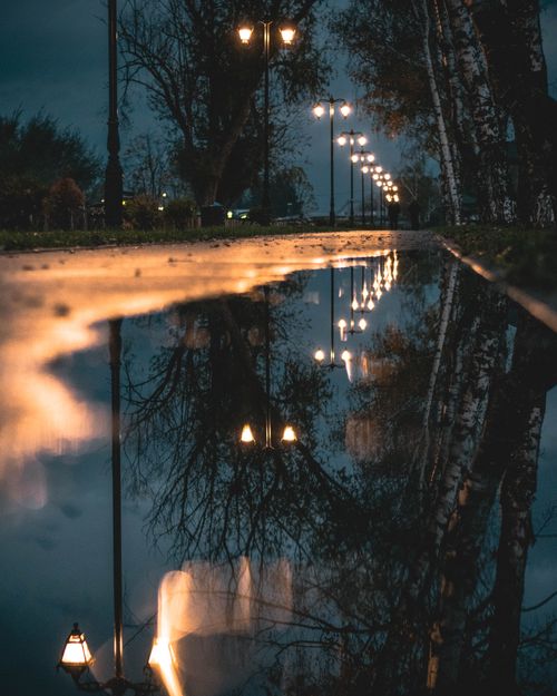 Free A tranquil park scene with lamp reflections at twilight, creating a moody atmosphere. Stock Photo