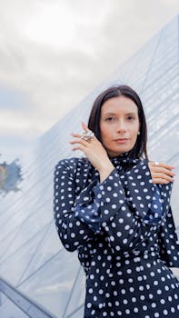 Elegant woman in polka dot dress poses by the Louvre Pyramid in Paris.