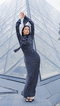 Fashionable woman posing in a polka dot dress near the iconic Louvre Pyramid in Paris.