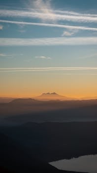 A tranquil sunset scene over mountain ranges with a clear sky and contrails.