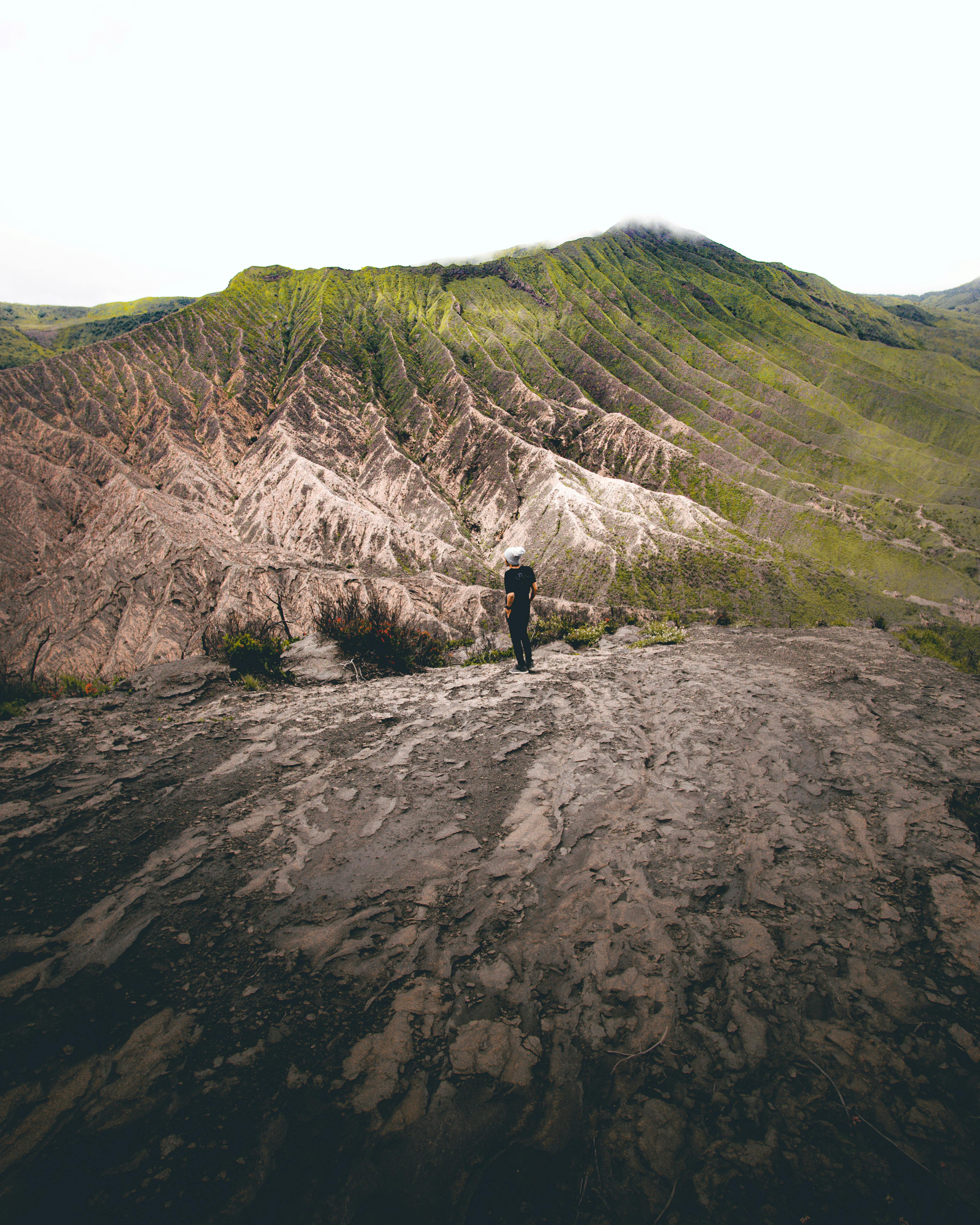 A lone hiker stands on a rugged volcanic terrain, showcasing breathtaking natural beauty.