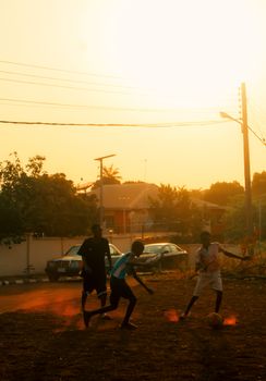 Children play soccer on a dusty street during a warm sunset in Enugu, Nigeria.