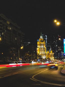 Vibrant city skyline at night, showcasing light trails from speeding cars and illuminated buildings.