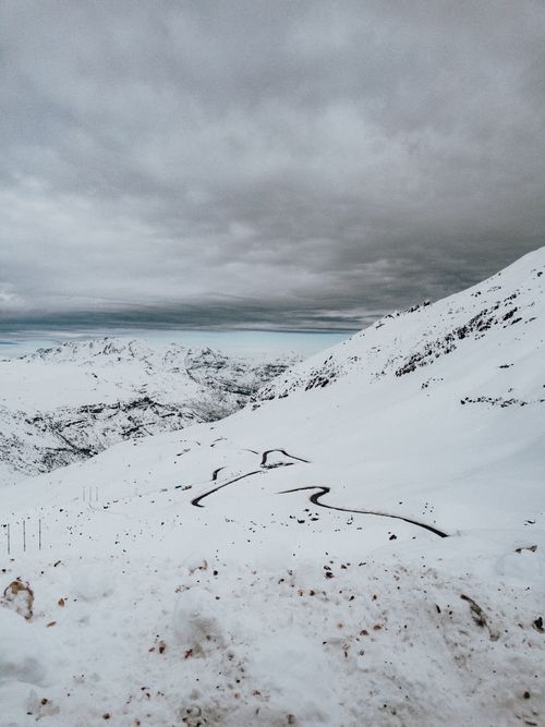 Free Scenic snowy mountain road twisting through a serene winter landscape under cloudy skies. Stock Photo