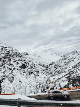 A car driving along a snow-covered mountain road with scenic winter landscape.