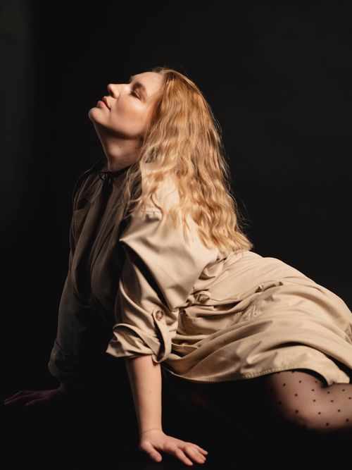 Free Artistic portrait of a woman in a beige trench coat, striking a graceful pose against a dark background. Stock Photo