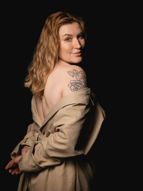 Free Artistic portrait of a woman showcasing floral tattoo and trench coat on black background. Stock Photo