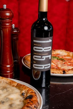 Artisanal pizza and red wine bottle on a table in a cozy setting.