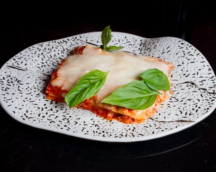 Savory lasagna with melted cheese and fresh basil leaves, presented on an artistic plate.