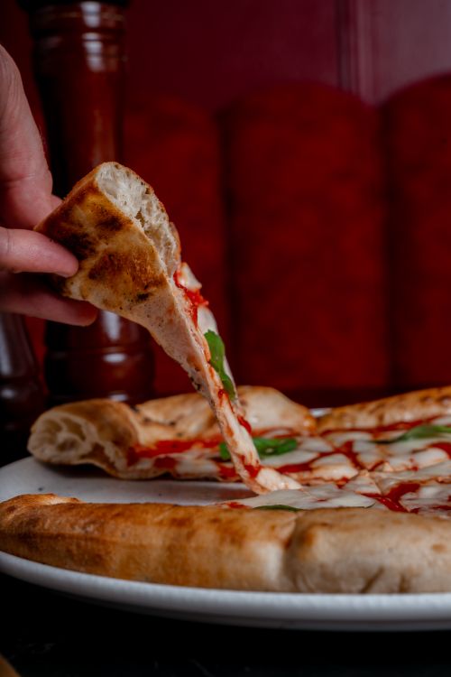 Free Hand lifting a tasty Margherita pizza slice with melted cheese in a cozy setting. Stock Photo