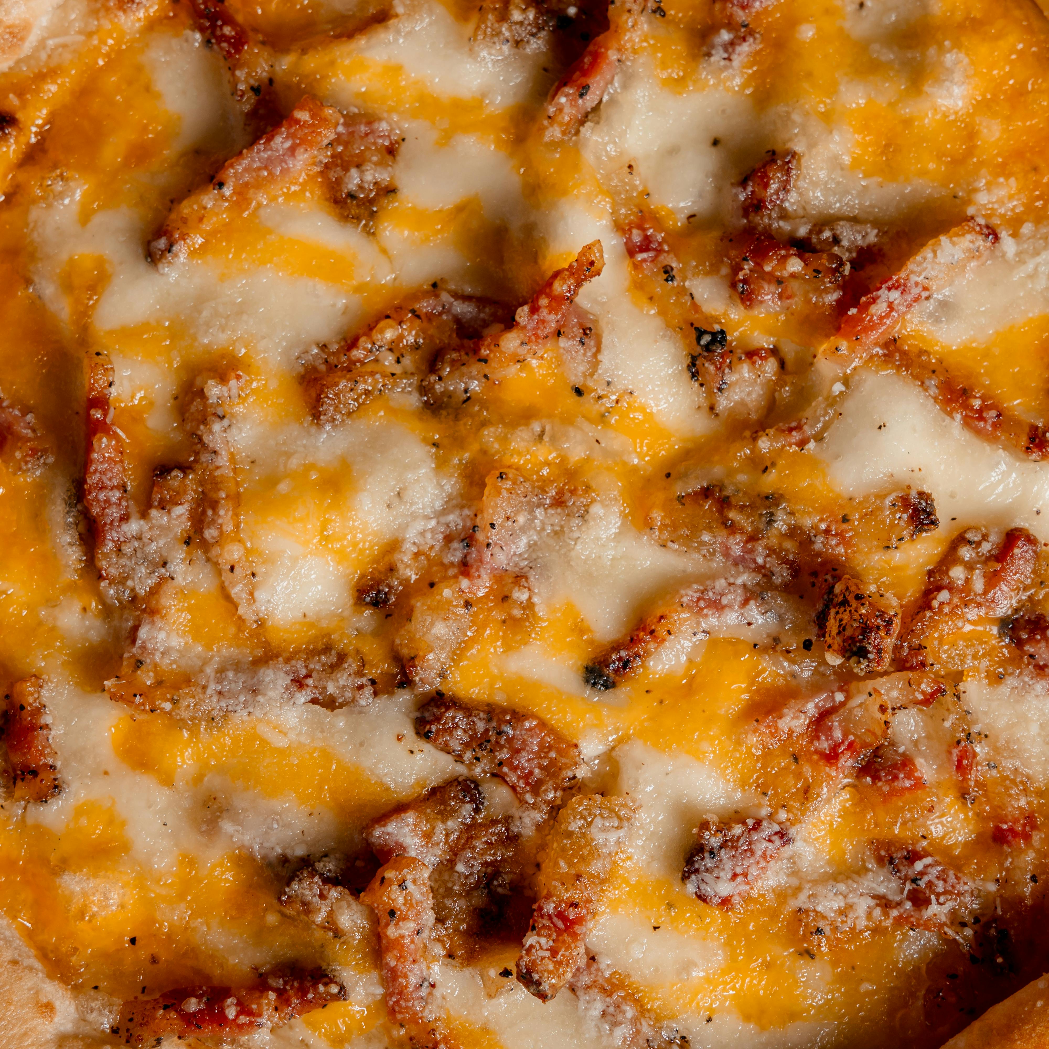 Close-up of a cheesy artisanal pizza topped with cheddar and crispy bacon in Islas Baleares, España.