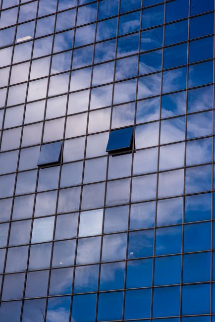 A contemporary glass facade reflecting clouds and blue skies, showcasing urban architecture.