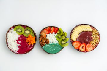 Three coconut shell smoothie bowls with dragon fruit, spirulina, kiwi, banana and strawberries