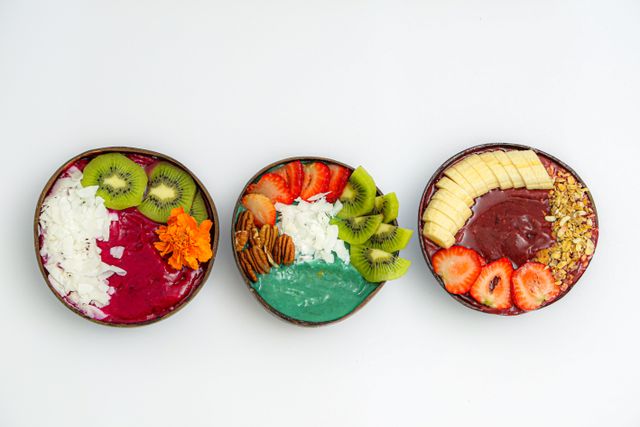 Three coconut shell smoothie bowls with dragon fruit, spirulina, kiwi, banana and strawberries
