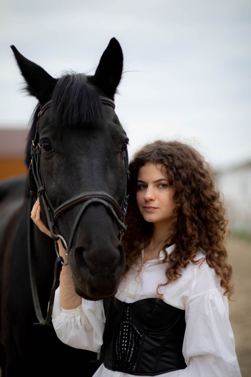 Free A young woman standing with a black horse outdoors, portraying companionship. Stock Photo