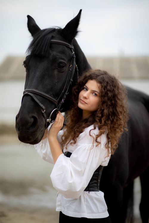 Free A young woman gently holding a black horse outdoors. Stock Photo