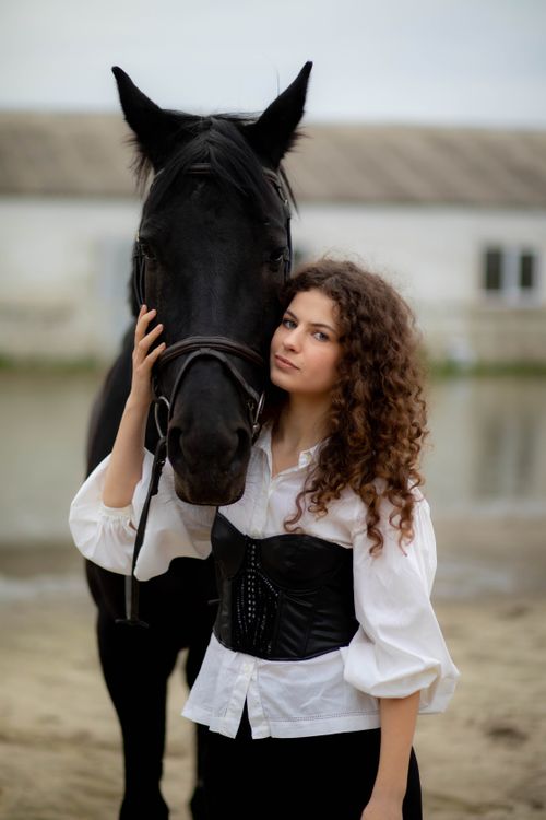 Free A young woman in a white blouse and corset posing with a black horse by her side. Stock Photo