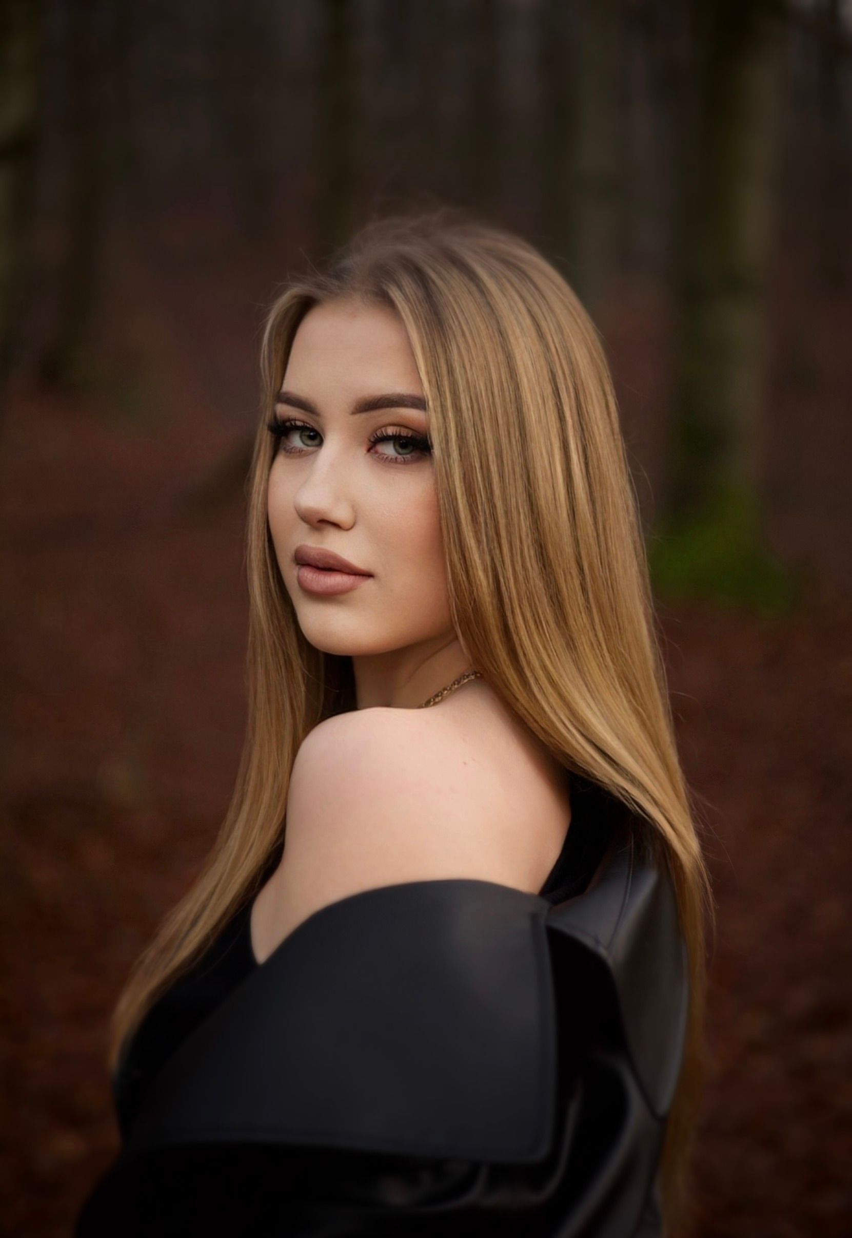 Portrait of a young woman with long hair in an autumn forest, wearing a stylish leather jacket.