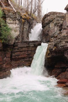 Majestic waterfall cascading through rocky cliffs surrounded by forest in Glacier National Park.