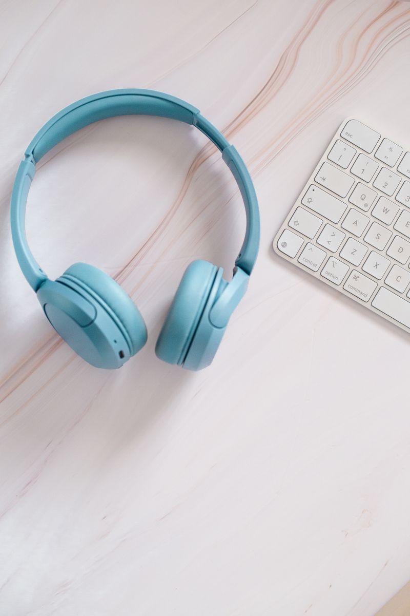 Minimalist workspace with blue headphones and a white keyboard on a desk