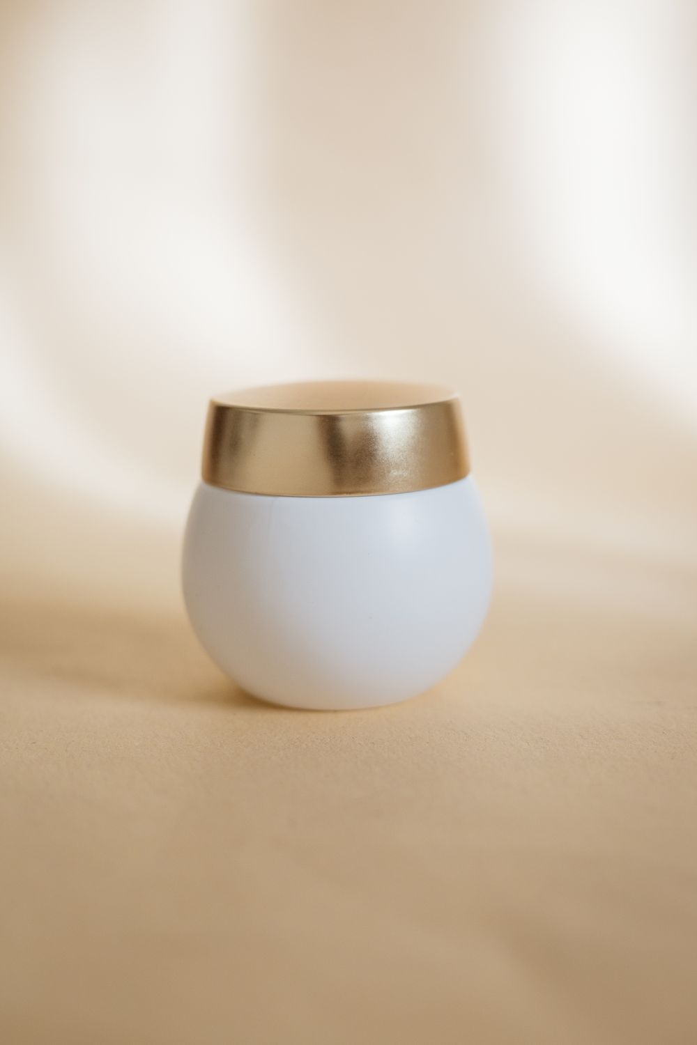 Minimal white skincare jar with a champagne-gold lid