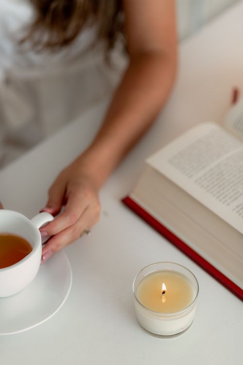 Free Cozy scene of a person enjoying tea and reading a book by candlelight. Stock Photo