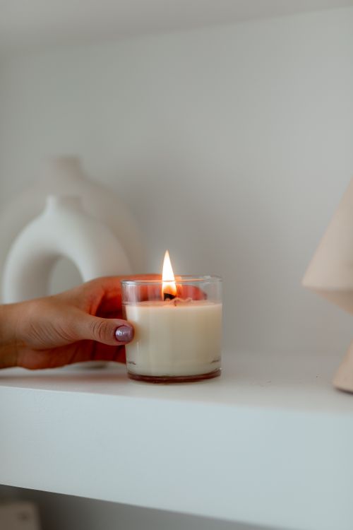 Free A hand with painted nails lights a white candle in a minimalist indoor setting. Stock Photo