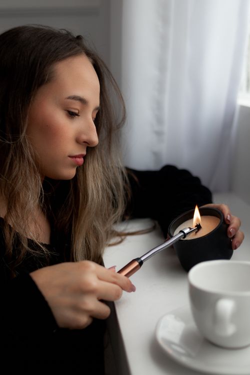 Free Woman with long hair lighting a candle indoors. Cozy, calm atmosphere. Stock Photo