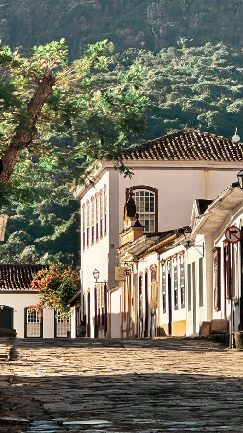 Free Sunlit colonial street in a historic town with cobblestones and lush greenery. Stock Photo