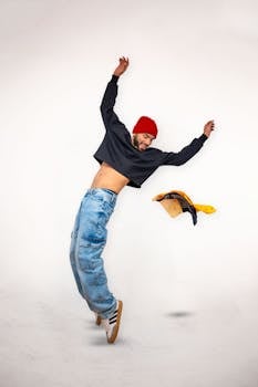 A young man energetically poses in a studio, wearing jeans and a red hat, showcasing modern fashion.
