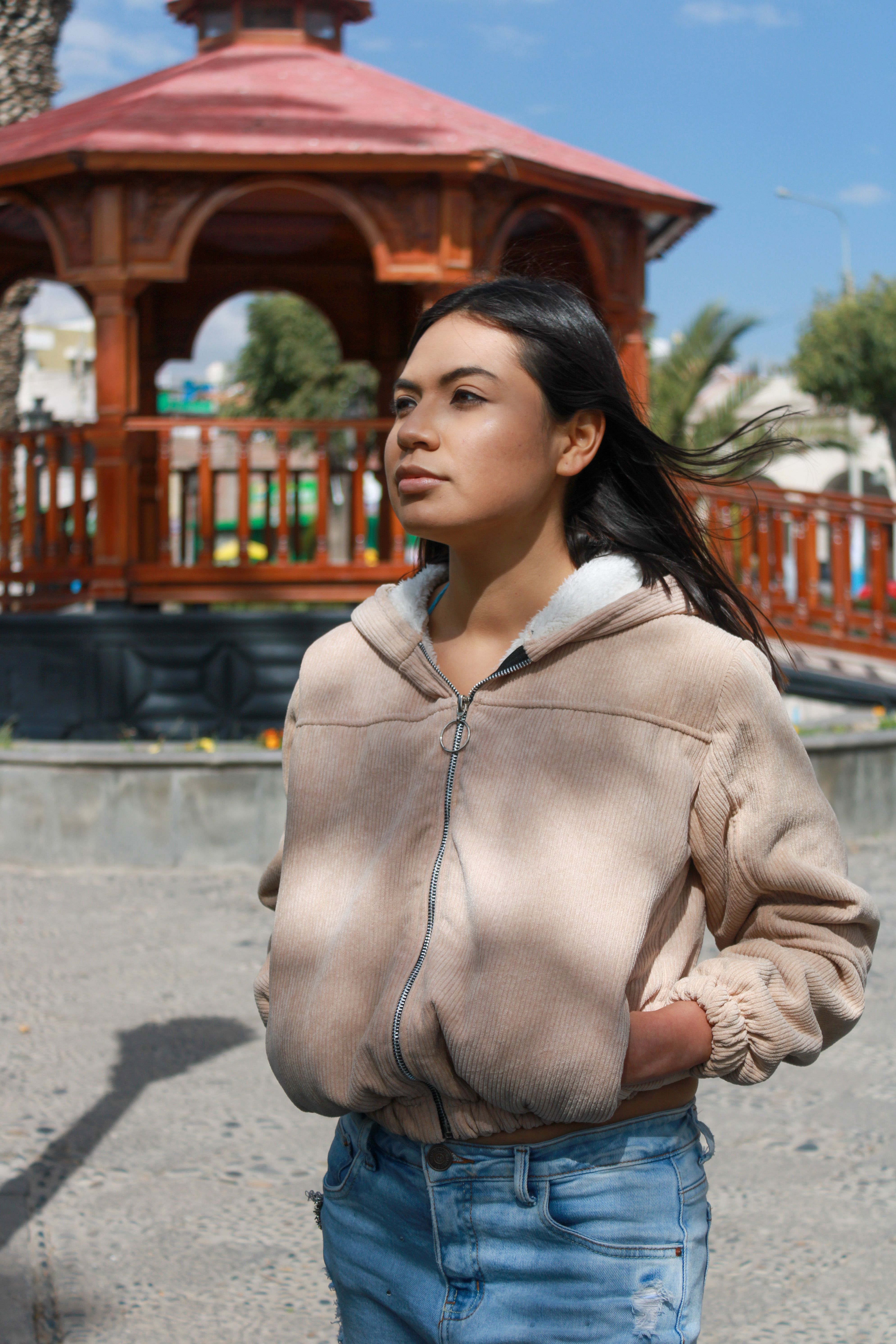 Casual portrait of a young woman in a plaza, facing away with sunny backdrop.