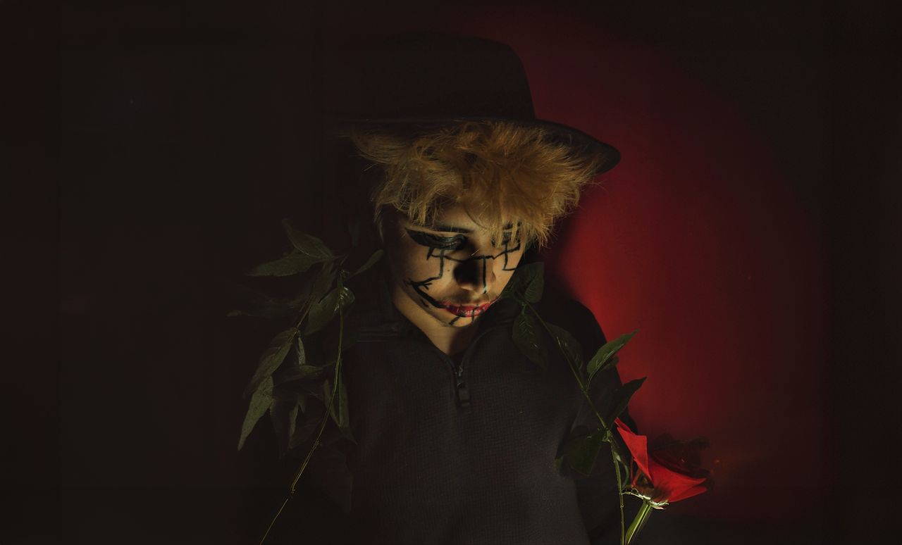 a person with a scarecrow inspired painted face holding a red rose in