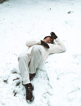 Man lying on snow-covered ground enjoying a peaceful winter day.