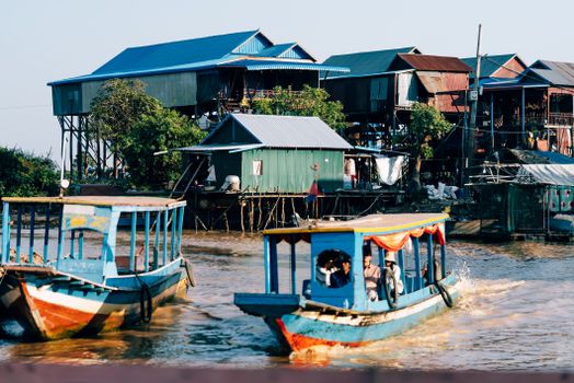 Colorful boats navigate near stilt houses in a vibrant riverside village.