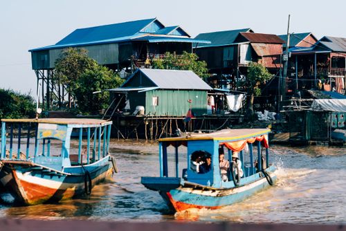 Free Colorful boats navigate near stilt houses in a vibrant riverside village. Stock Photo