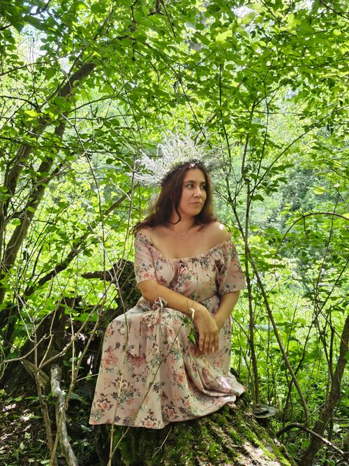 Free Woman in a floral dress with a jeweled crown sitting in a lush green forest. Stock Photo