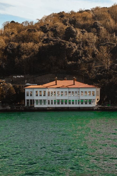 Free Elegant white mansion by a turquoise body of water with lush autumn foliage. Stock Photo
