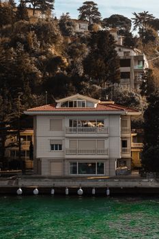 Scenic view of a modern villa by a green lake surrounded by lush trees.