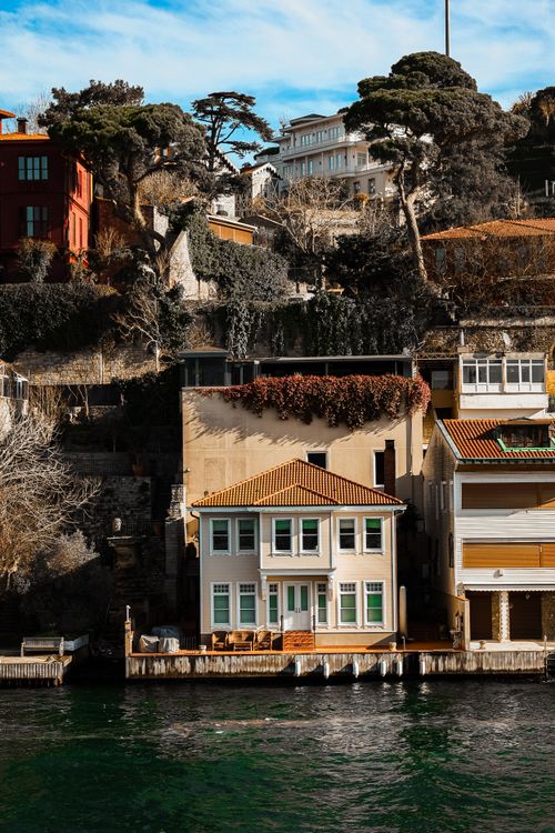 Free Scenic waterfront house nestled against a cliff with lush trees and neighboring homes. Stock Photo