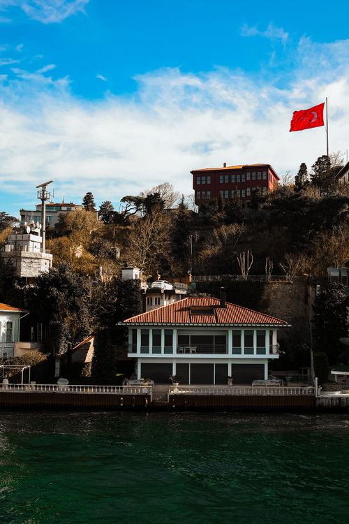 Free A red flag waves high above elegant waterfront buildings under a clear blue sky. Stock Photo