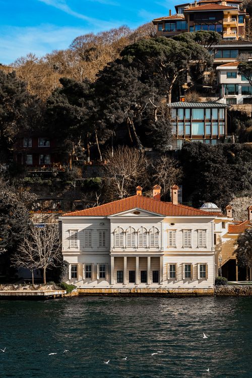 Free Charming villa by a tranquil lake with lush hillside backdrop. Stock Photo
