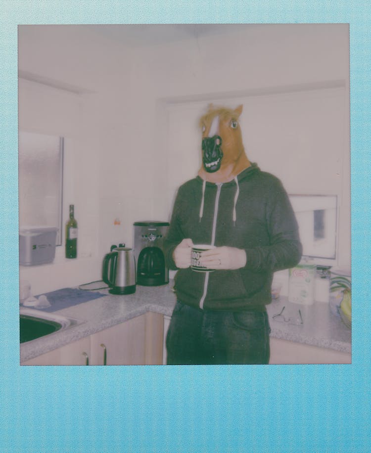 A Tall Person Wearing A Horse Mask Holding A Mug In The Kitchen