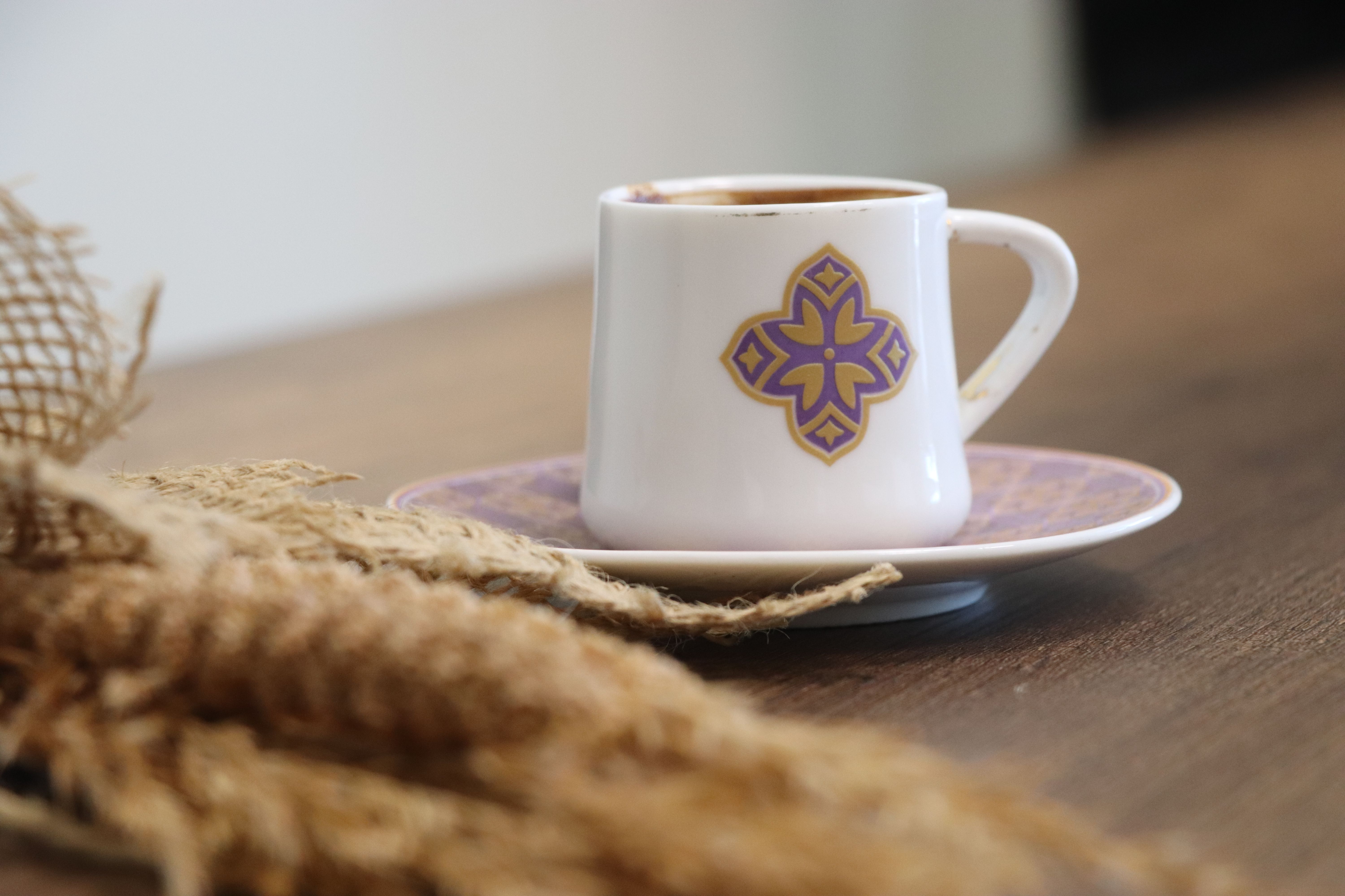 A traditional Turkish coffee served in a decorated cup, on a rustic wooden table with an artistic touch.