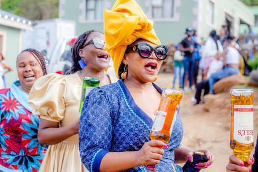Three women in colorful attire enjoying an outdoor celebration with drinks and laughter.