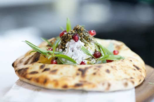 Tantalizing flatbread topped with creamy cheese, herbs, and pomegranate seeds.