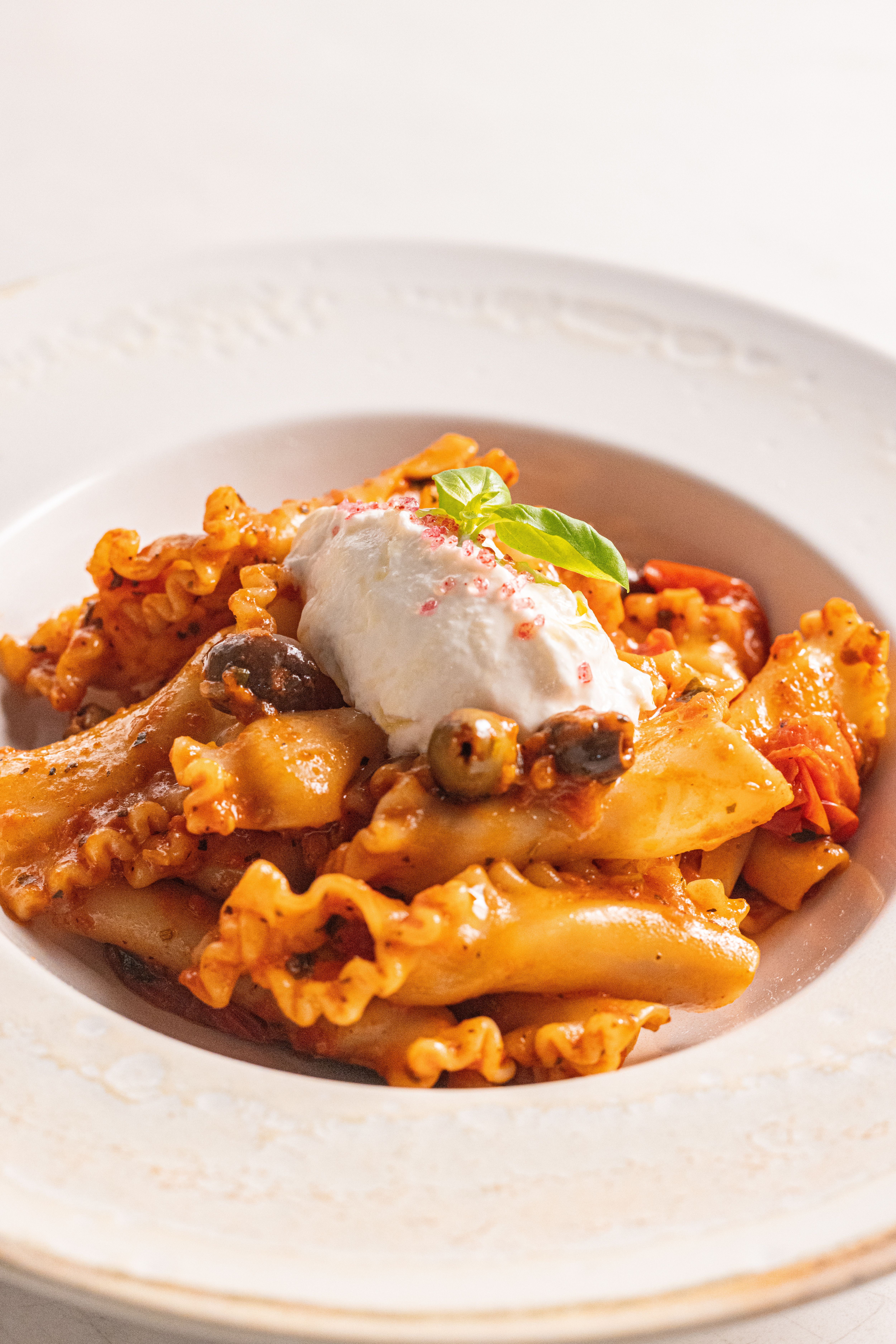 Appetizing Mafaldine pasta dish with ricotta cheese and olives in a restaurant setting.