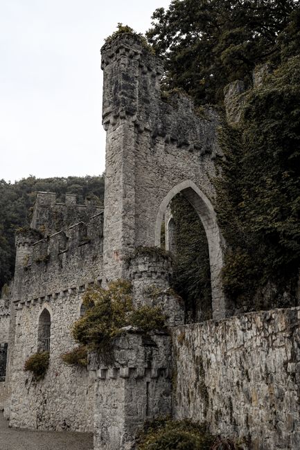 A historic stone castle wall with ancient arched entry and lush greenery.