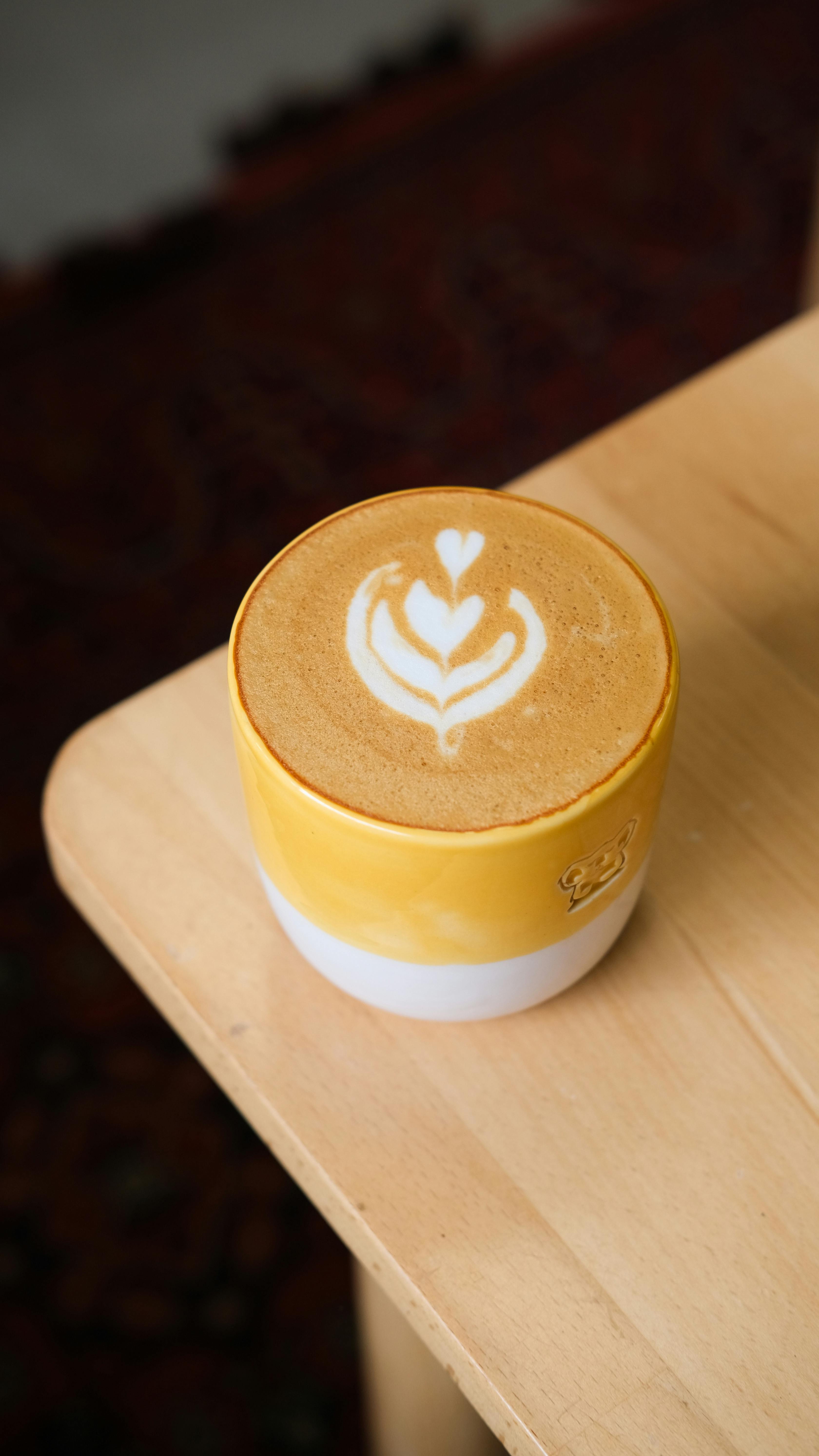Close-up of cappuccino with latte art in a yellow cup on a wooden table.