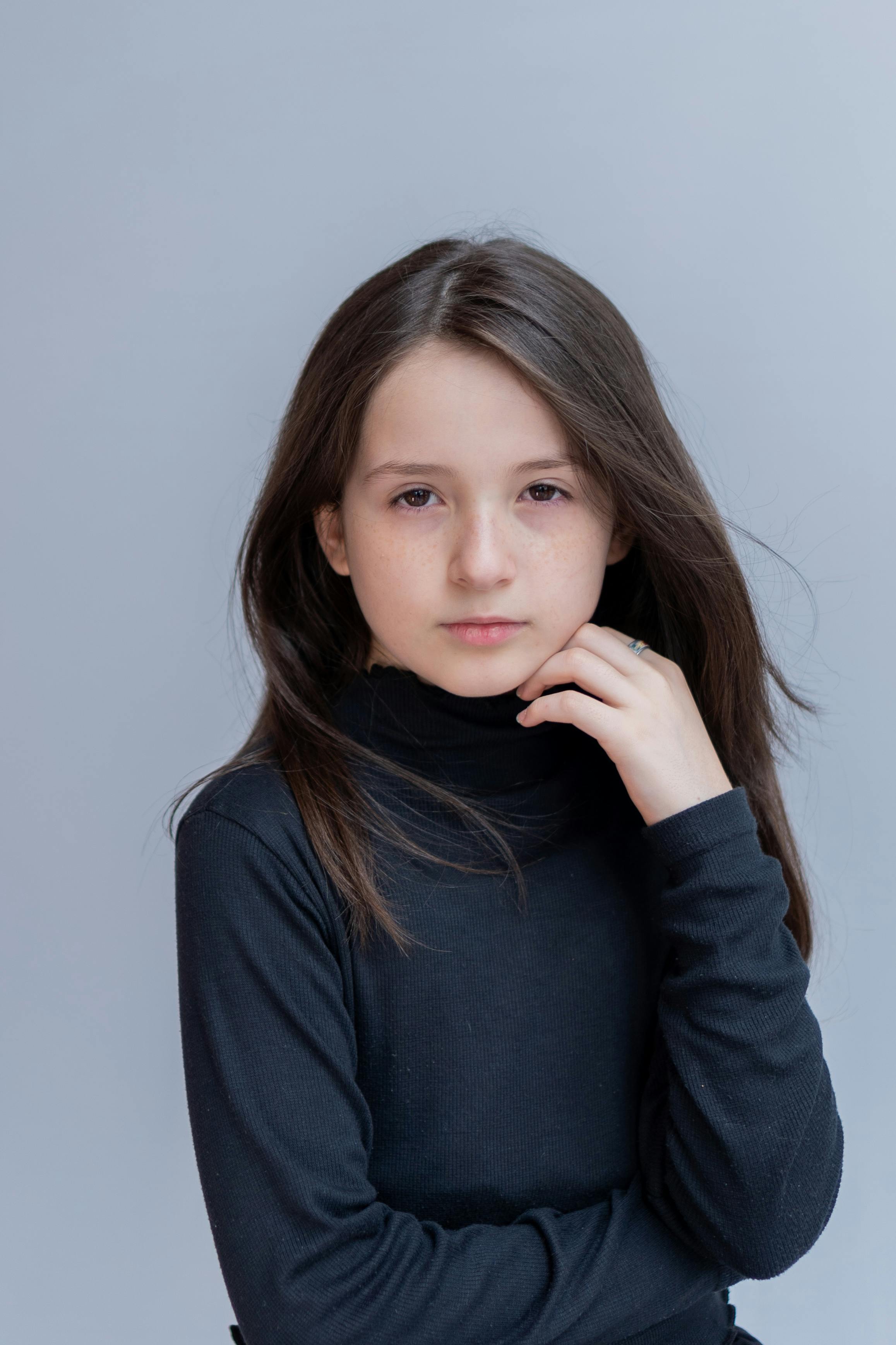 A young girl in a black turtleneck gazes thoughtfully at the camera.